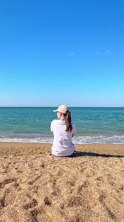 Back view girl is sitting on the sand on the seashore, relaxing and enjoying  Stock Footage 305872852