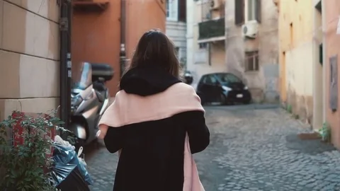 Back view of girl walking alone in old town. Brunette woman going through the Stock Footage 73479897