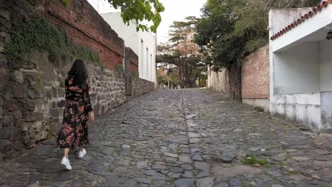 Back view of girl walking down cobblestone street, Uruguay. Tracking shot, Stock Footage 131103129