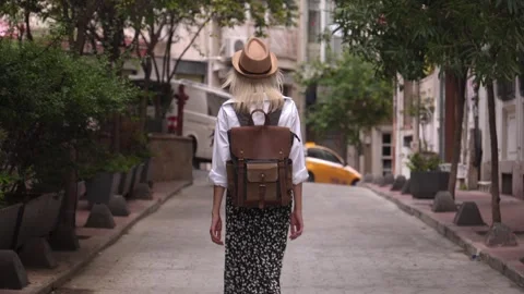 Back view of girl walking down city street with backpack in hat Stock Footage 252929741
