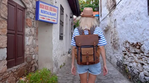 Back view of girl walking down city street with backpack in hat Vídeos de archivo 253300989
