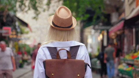 Back view of girl walking down city street with backpack in hat Stock Footage 253303909