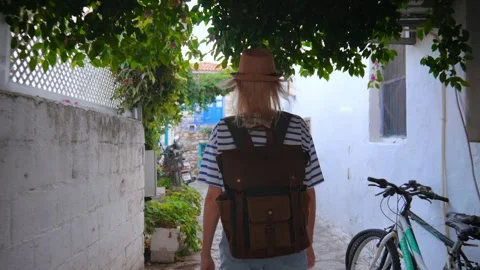 Back view of girl walking down city street with backpack in hat Stock Footage 253303944