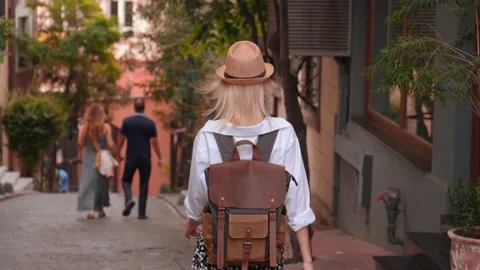 Back view of girl walking down city street with backpack in hat Vidéo 253304102