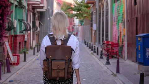 Back view of girl walking down city street with backpack in hat Video stock 253305495