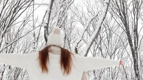 Back view, a girl in a white hat, scarf and sweater walks in a snowy park Stock Footage 253088992