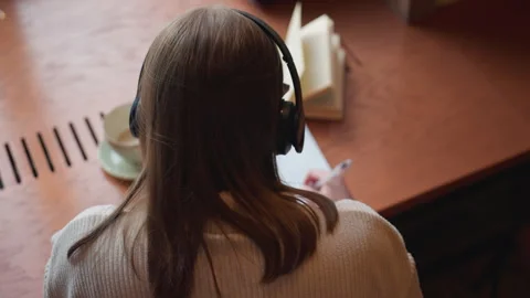 Back view of girl writing with coffee cup beside and novel dancing to music Stock Footage 310752280