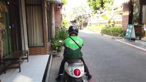 Back View of Grab Delivery Driver Seated on Scooter Checking Phone in Ubud Stock Footage 342296788