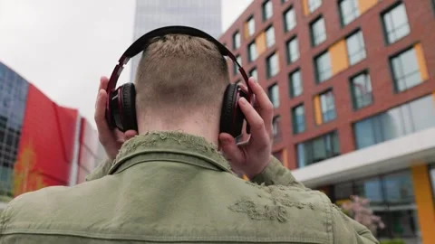 Back view of guy wearing headphones and listening to music outdoors Stock Footage 323925631