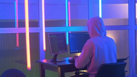 Back view of Hacker in white hoodie penetrating network system in neon room Video stock 130656099