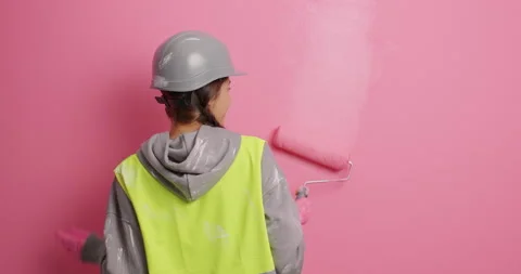 Back view of happy female painter dances while applying paint on wall uses Stock Footage 155492365
