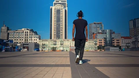 Back view hipster guy listen music walks in town Stock Footage 119585365