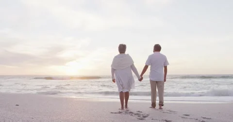 Back view of hispanic just married senior couple walking on beach at sunset Stock Footage 337699431