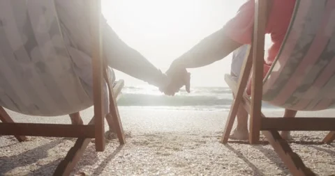 Back view of hispanic senior couple relaxing on sunbed on beach at sunset, Stock Footage 336436007