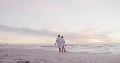 Back view of hispanic senior couple walking on beach at sunset Stock Footage 344252301