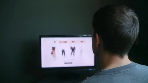 Back view of individual sitting at table with computer, exploring fashion site Stock Footage 312846244