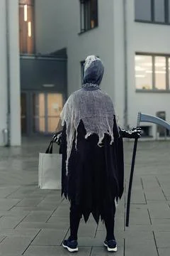 Back view of kid in grim reaper Halloween costume with scythe and bag for sweets Stock Photos