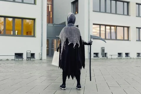 Back view of kid in grim reaper Halloween costume with scythe and bag for sweets Stock Photos
