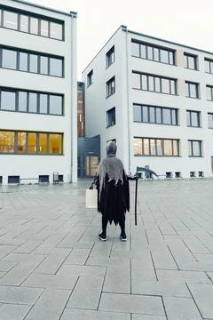 Back view of kid in grim reaper Halloween costume with scythe and bag for sweets Stock Photos