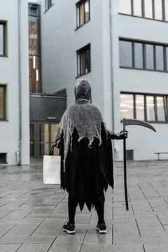 Back view of kid in grim reaper Halloween costume with scythe and bag for sweets Fotos de archivo