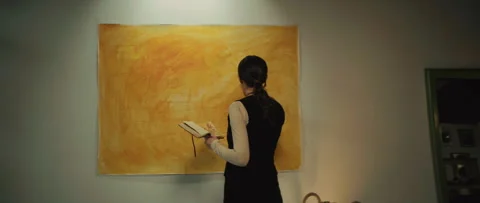 Back view of lady artist standing beside yellow artwork in art space. Young Stock Footage 277580731
