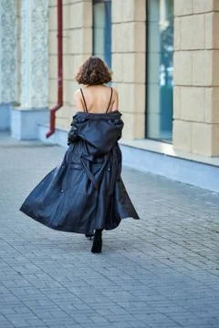 Back view of a lady walking down the street and taking off leather coat Stock Photos