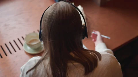 Back view of lecturer writing with coffee beside and novel dancing to music Stock Footage 310752298