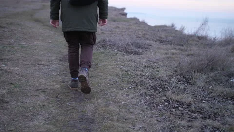Back view a legs of man walking a dirty green hills above the sea. Stock Footage 151607048