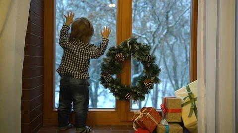 Back view of the little blond boy looking through decorated window with wreath Stock Footage 86868087