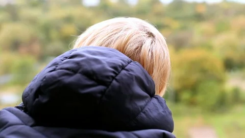 Back view of little blonde boy looking out of the window with green nature on bl Vidéo 117471986