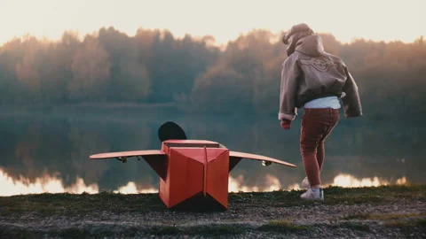 Back view little boy in old pilot costume sitting at amazing forest lake with Video stock 99693325