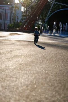 Back view of little boy running in sunny amusement park near fountains, happy ch Stock Photos