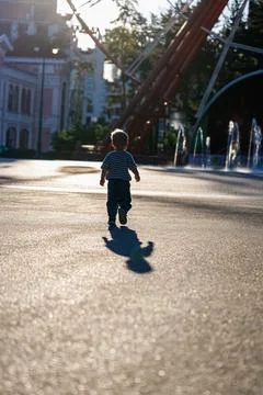 Back view of little boy running in sunny amusement park near fountains, happy ch Stock Photos