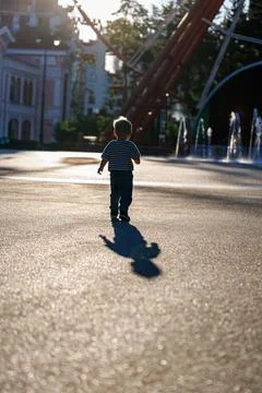 Back view of little boy running in sunny amusement park near fountains, happy ch Stock Photos
