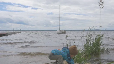 Back view of little boy standing on a beach and playng with sea foam in autumn Video stock 156672859