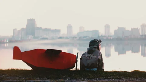 Back view of little pilot boy sitting near amazing peaceful city lake panorama Stock Footage 99693289