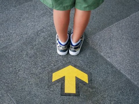 Back View of Low Section of Kid Standing In Front Of Yellow Directional Arrow Foto stock