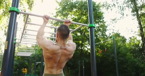 Back view of male athlete doing pull-up on horizontal bar outdoors while using Stock Footage 157402893