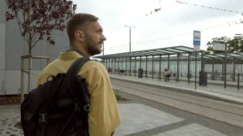Back view of male backpacker walking along bus stop sittin on bench Video stock 136135832