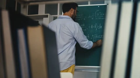 Back view of male math teacher writing exam task on chalkboard in classroom Stock Footage 311461641