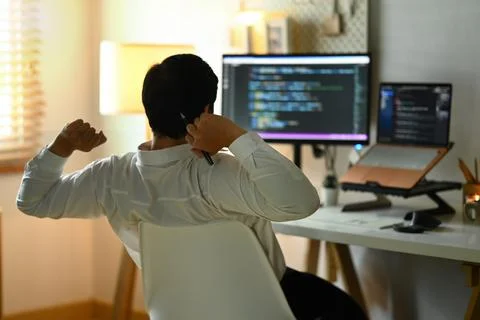 Back view of male programmer stretching arms and relaxing on chair at his Stock Photos