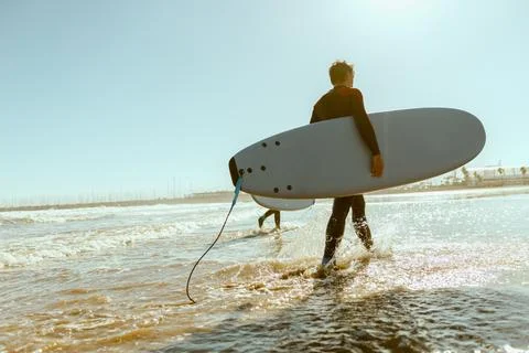 Back view of male surfer in wetsuit with his surfboard entering the sea. Surfing Stock Photos