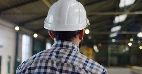 Back view on the male worker in a plaid shirt and a helmet walking in the Stock Footage 84406462