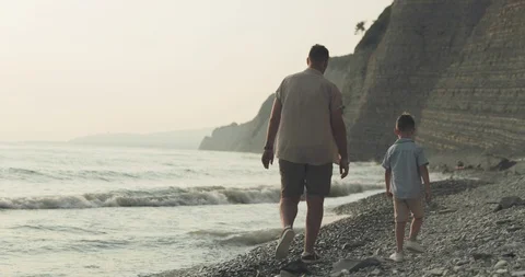 A back view of a man and a boy walking along a pebble beach Stock Footage 122430340