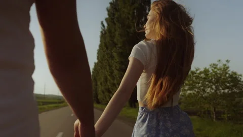 Back view of a man and redheaded woman walking on the road on a beautiful warm Stock Footage 253559641