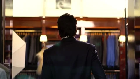 Back-view of man in blue jacket enters department selling luxury men's clothing 動画素材 260260859
