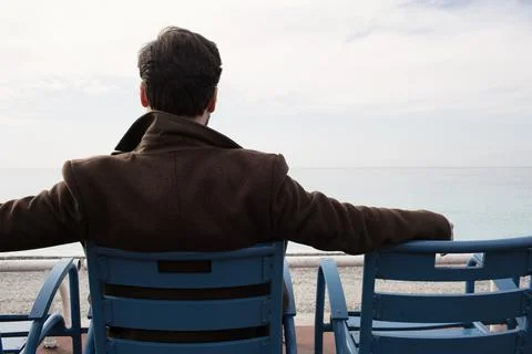 Back view of man in coat sitting on the bench against the sea coast. Cropped. 스톡 사진