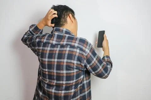 Back view of a man confused looking to the mobile phone that he hold Stock Photos