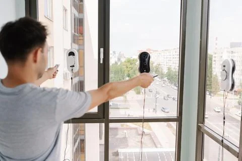 Back view of man controlling cleaning robots on skyscraper window using remote Stock Photos