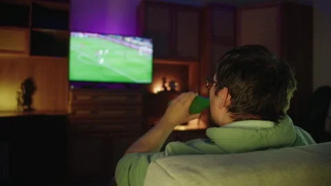 Back view of man drinks beer from glass bottle and watching football match on tv 库存影片 314396165